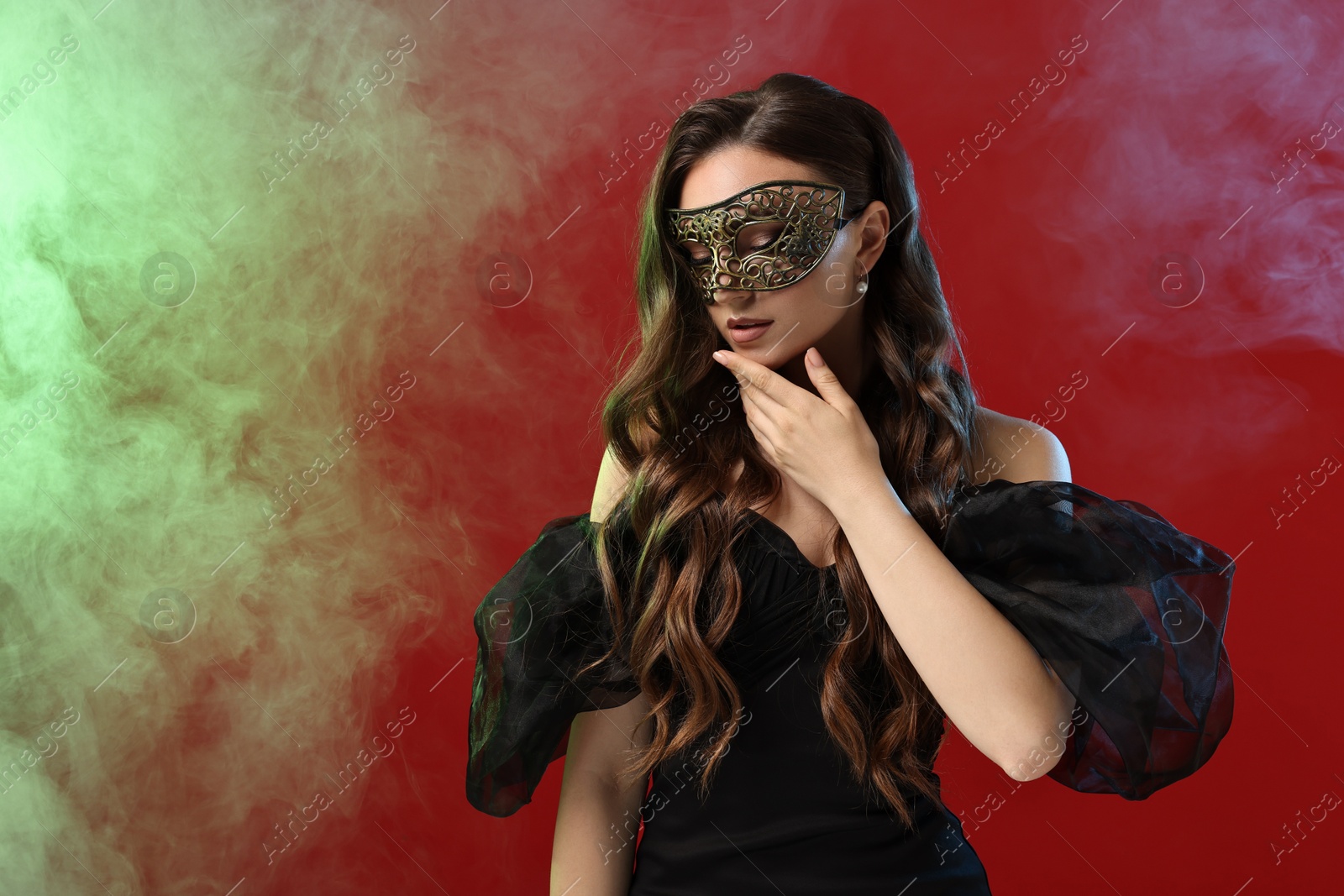 Photo of Beautiful woman wearing carnival mask on red background in color lights and smoke. Space for text