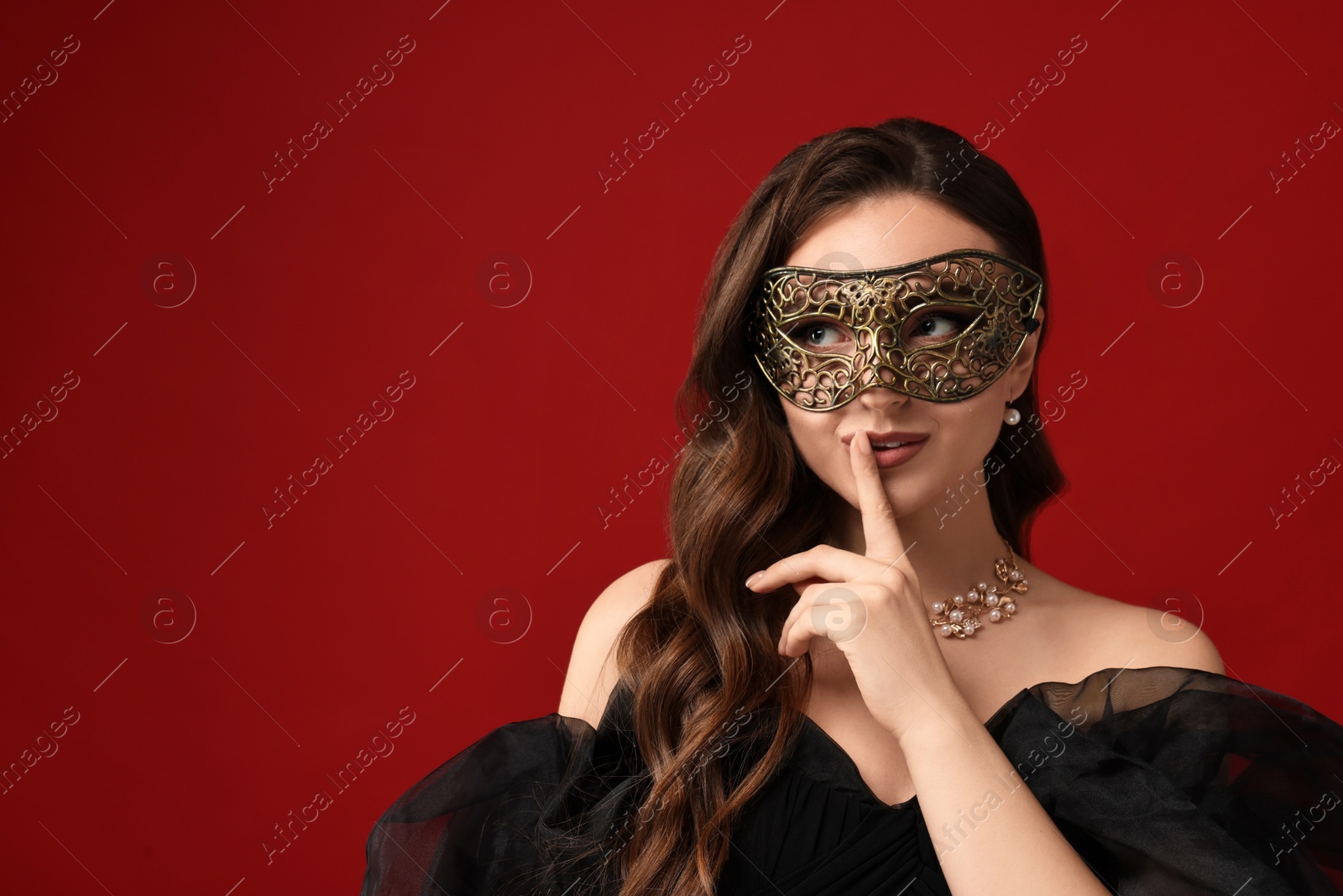 Photo of Beautiful woman with carnival mask showing hush gesture on red background. Space for text