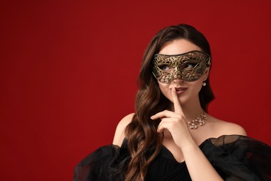 Photo of Beautiful woman with carnival mask showing hush gesture on red background. Space for text