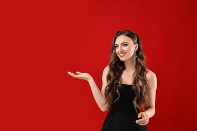 Portrait of smiling woman holding something on red background. Space for text