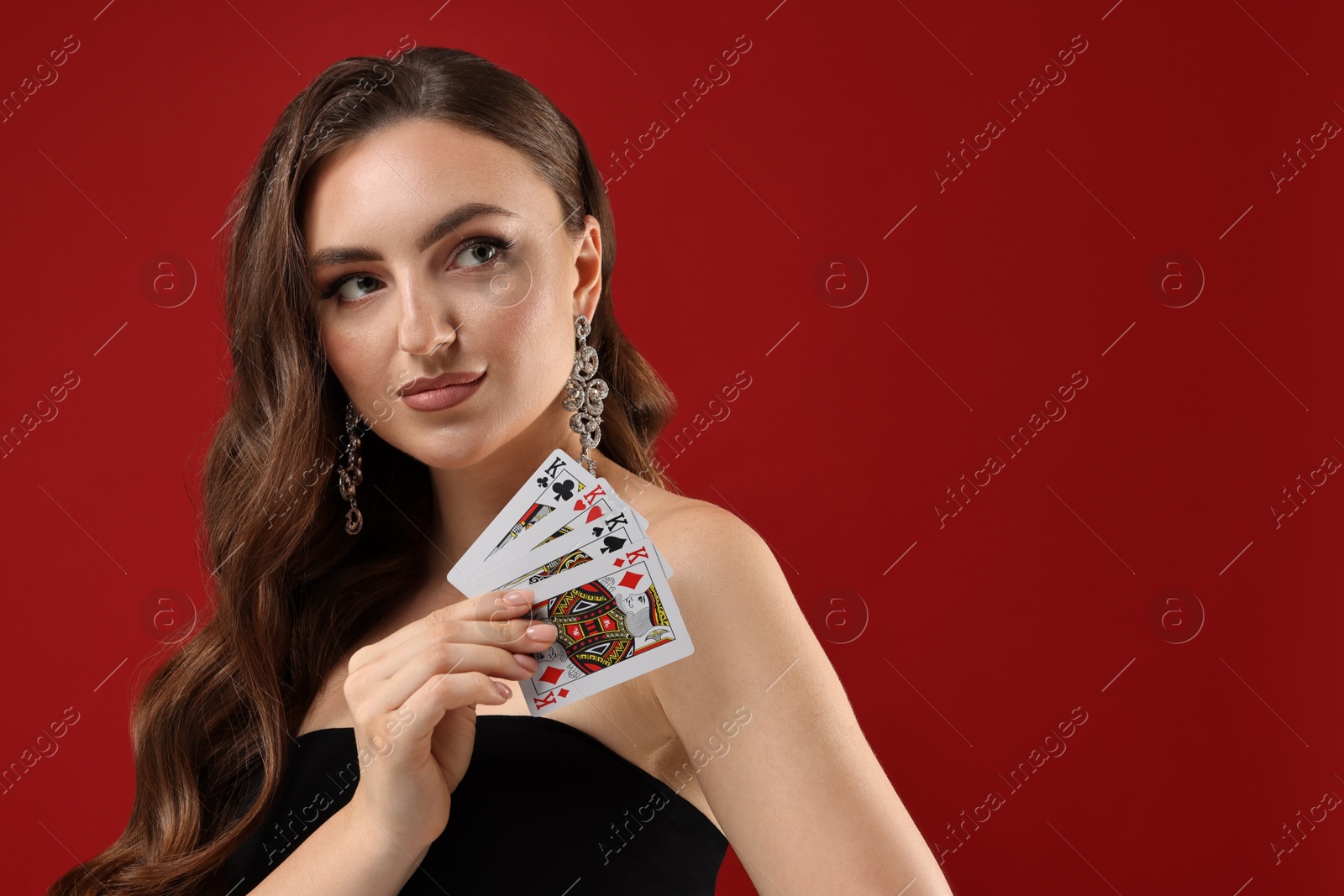 Photo of Poker game. Charming woman with playing cards on red background. Space for text