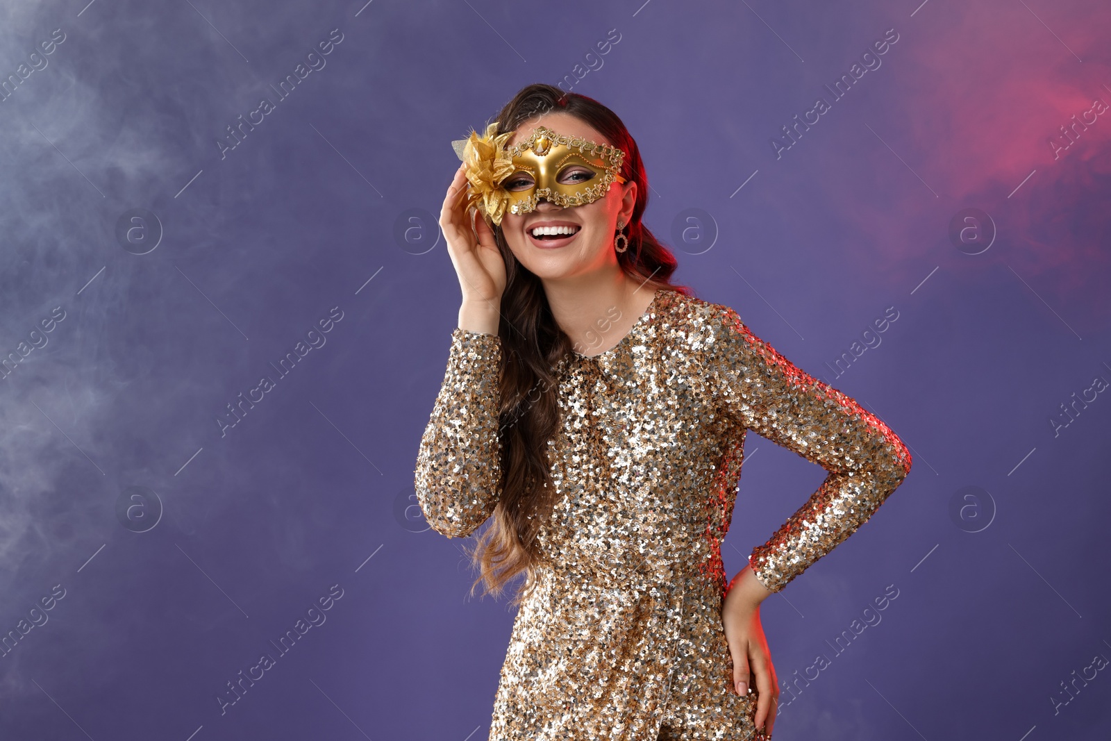 Photo of Smiling woman wearing carnival mask on purple background with smoke