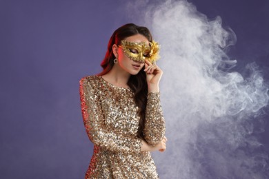 Photo of Beautiful woman wearing carnival mask on purple background with smoke