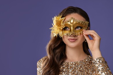 Photo of Beautiful woman wearing carnival mask on purple background, closeup. Space for text