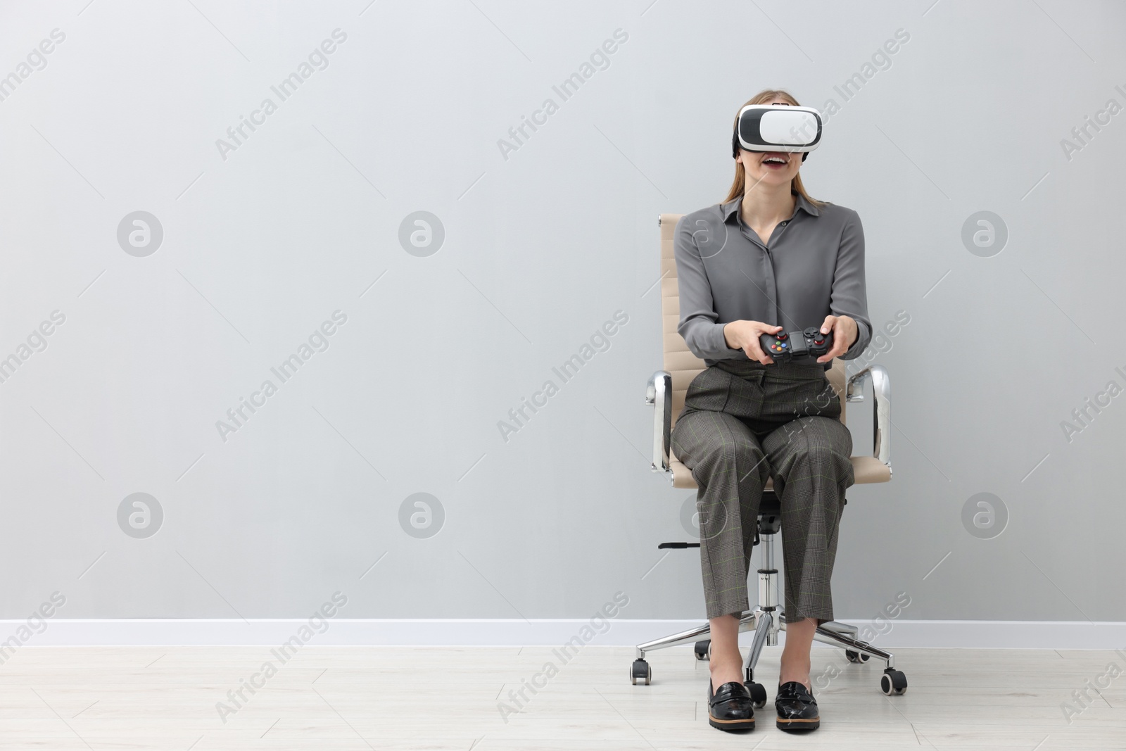 Photo of Happy woman with virtual reality headset and controller sitting on chair indoors, space for text