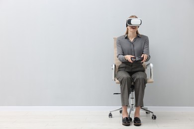 Photo of Happy woman with virtual reality headset and controller sitting on chair indoors, space for text