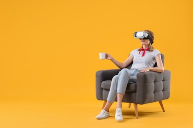 Surprised woman with virtual reality headset and cup sitting in armchair on yellow background, space for text