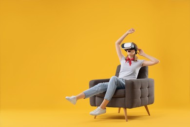 Emotional woman with virtual reality headset sitting in armchair on yellow background, space for text