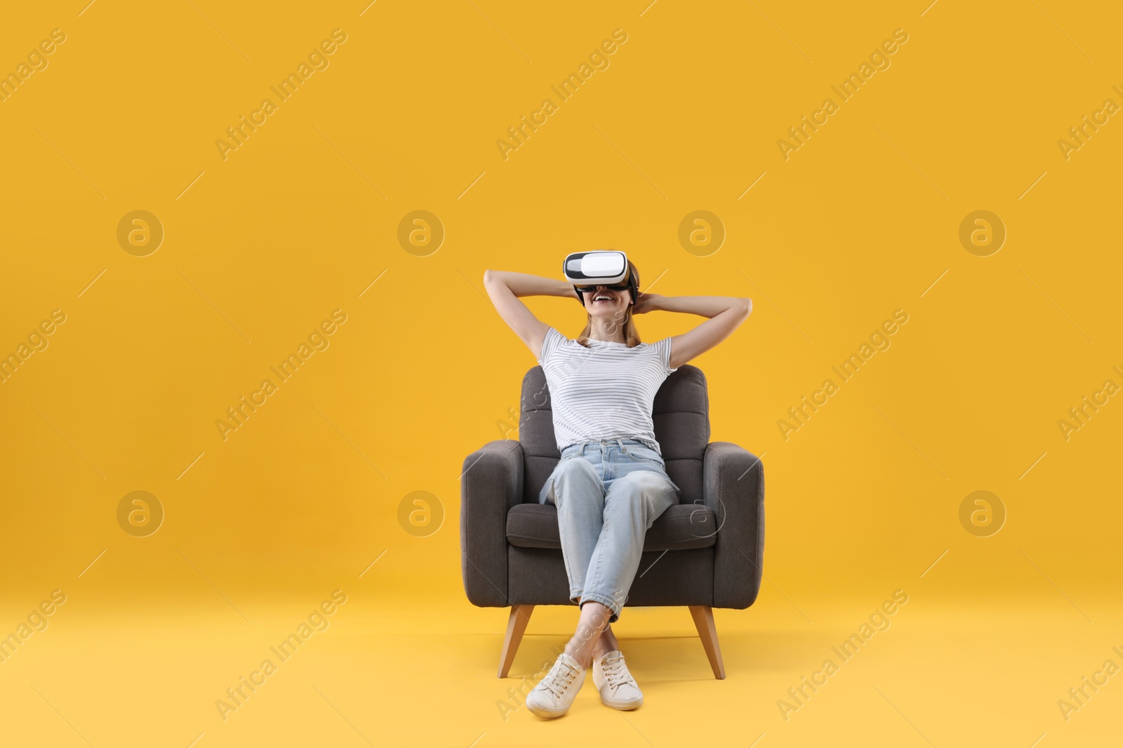 Photo of Happy woman with virtual reality headset sitting in armchair on yellow background