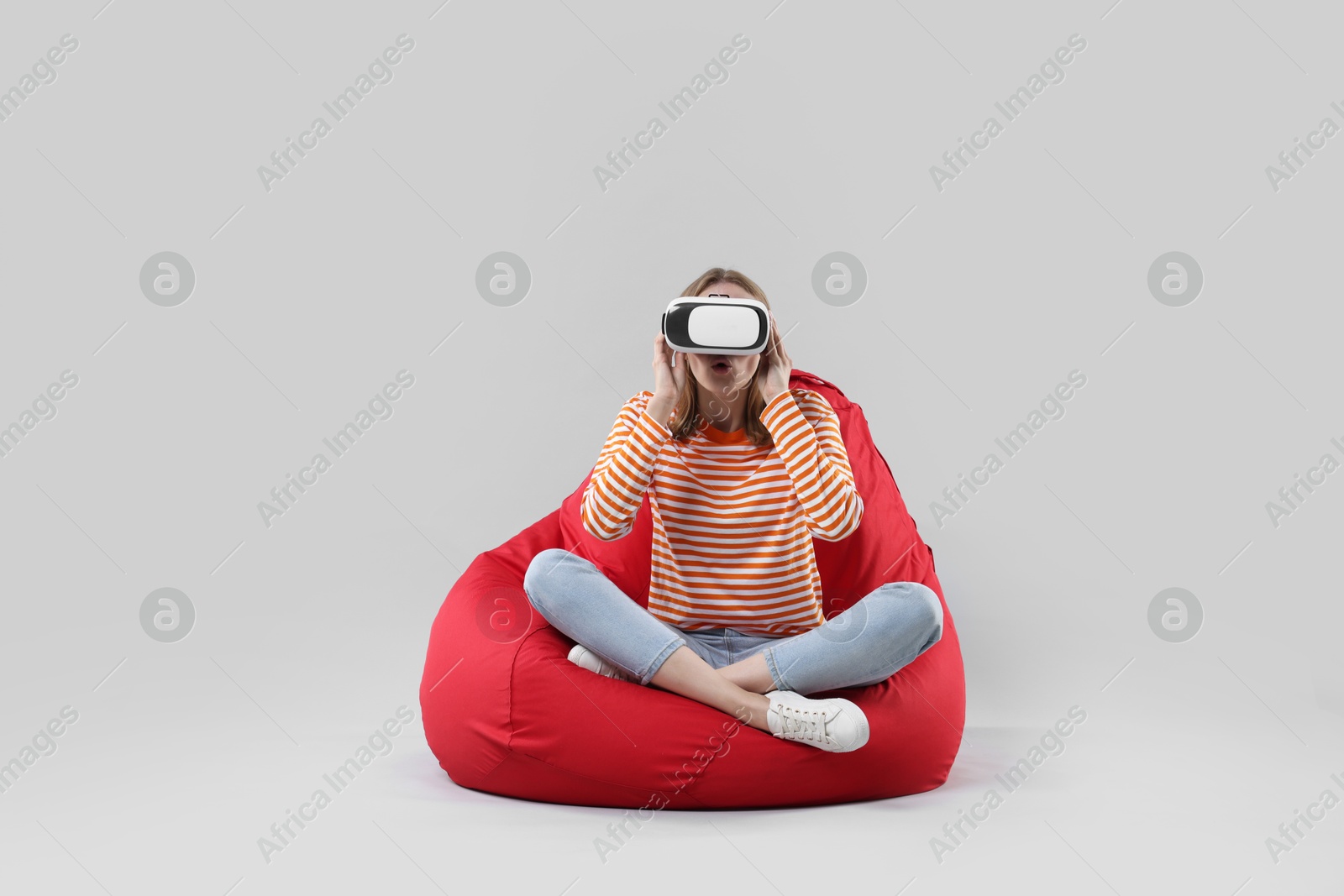 Photo of Emotional woman with virtual reality headset sitting on bean bag chair against gray background