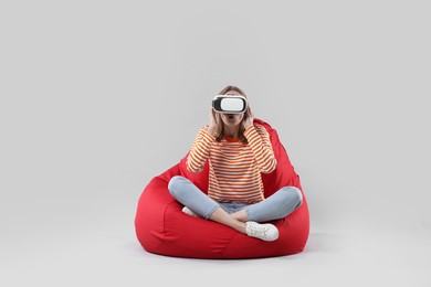 Photo of Emotional woman with virtual reality headset sitting on bean bag chair against gray background