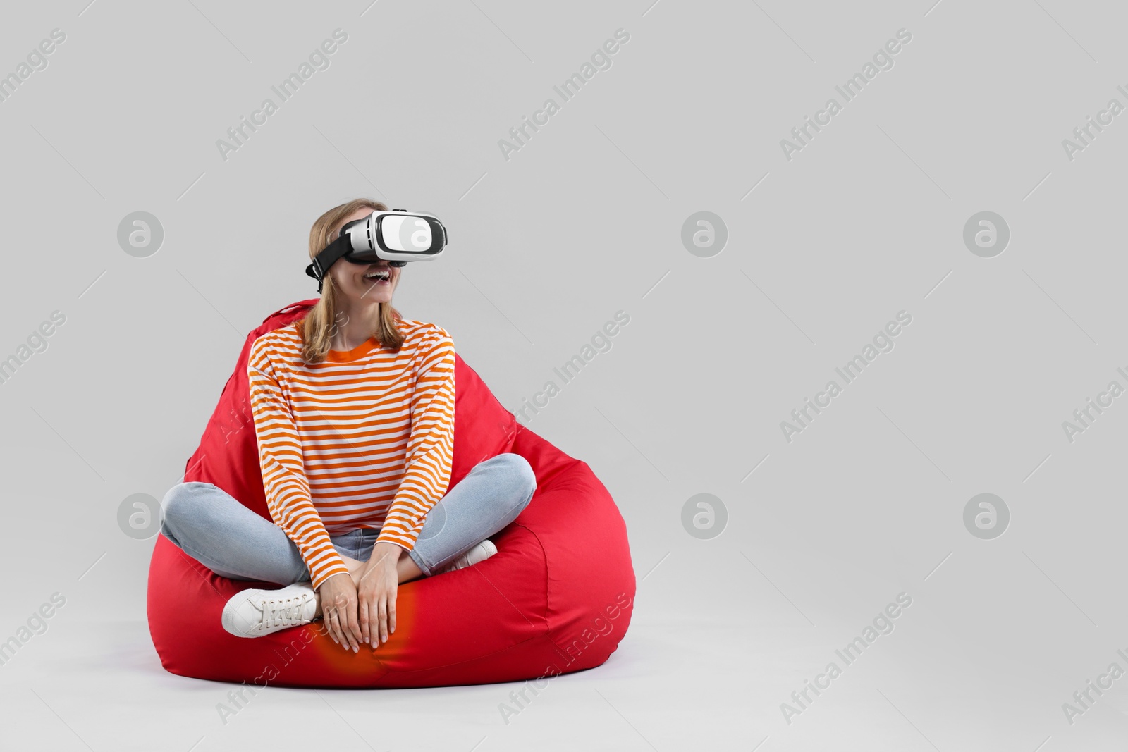 Photo of Happy woman with virtual reality headset sitting on bean bag chair against gray background, space for text