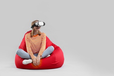 Happy woman with virtual reality headset sitting on bean bag chair against gray background, space for text