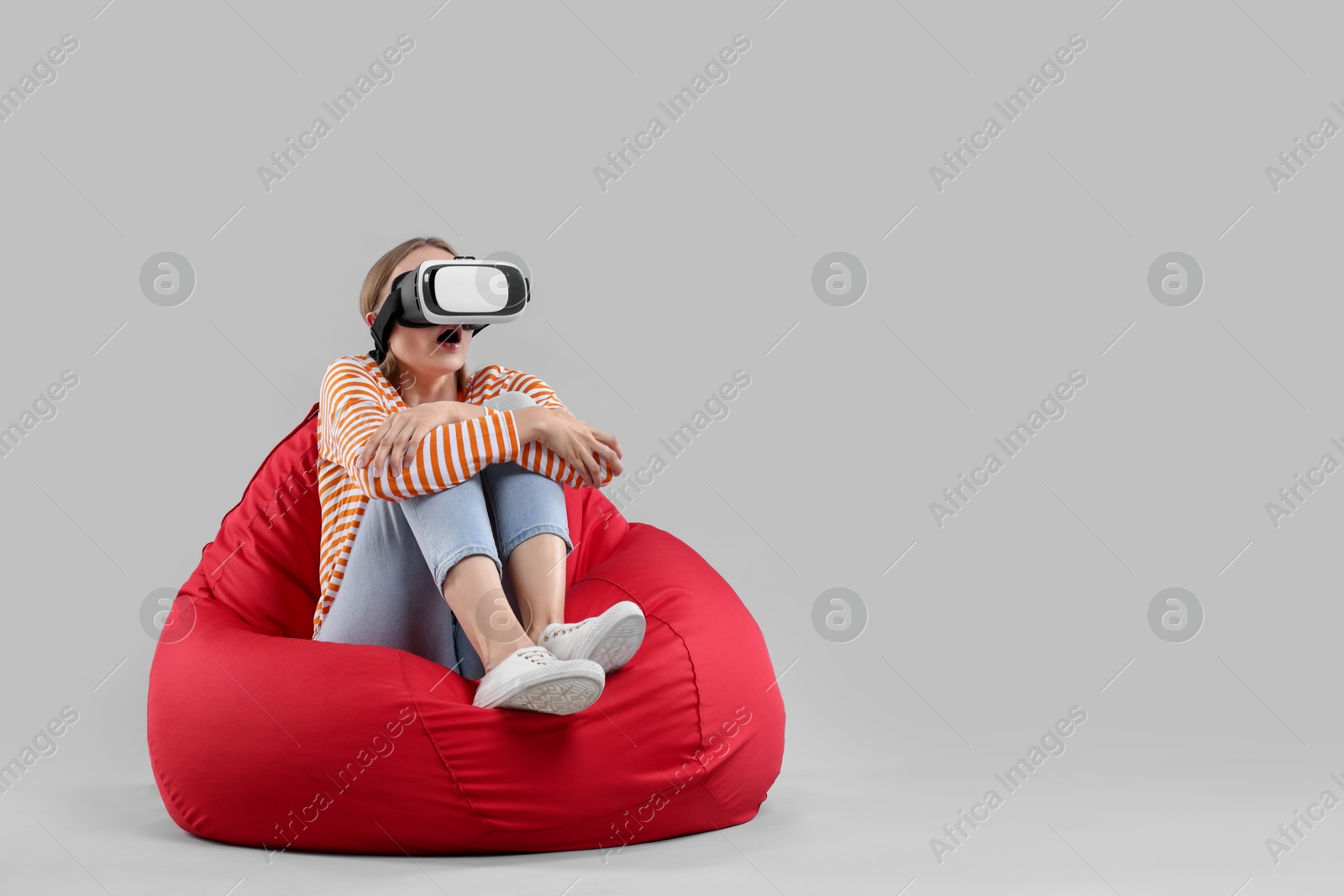 Photo of Emotional woman with virtual reality headset sitting on bean bag chair against gray background, space for text