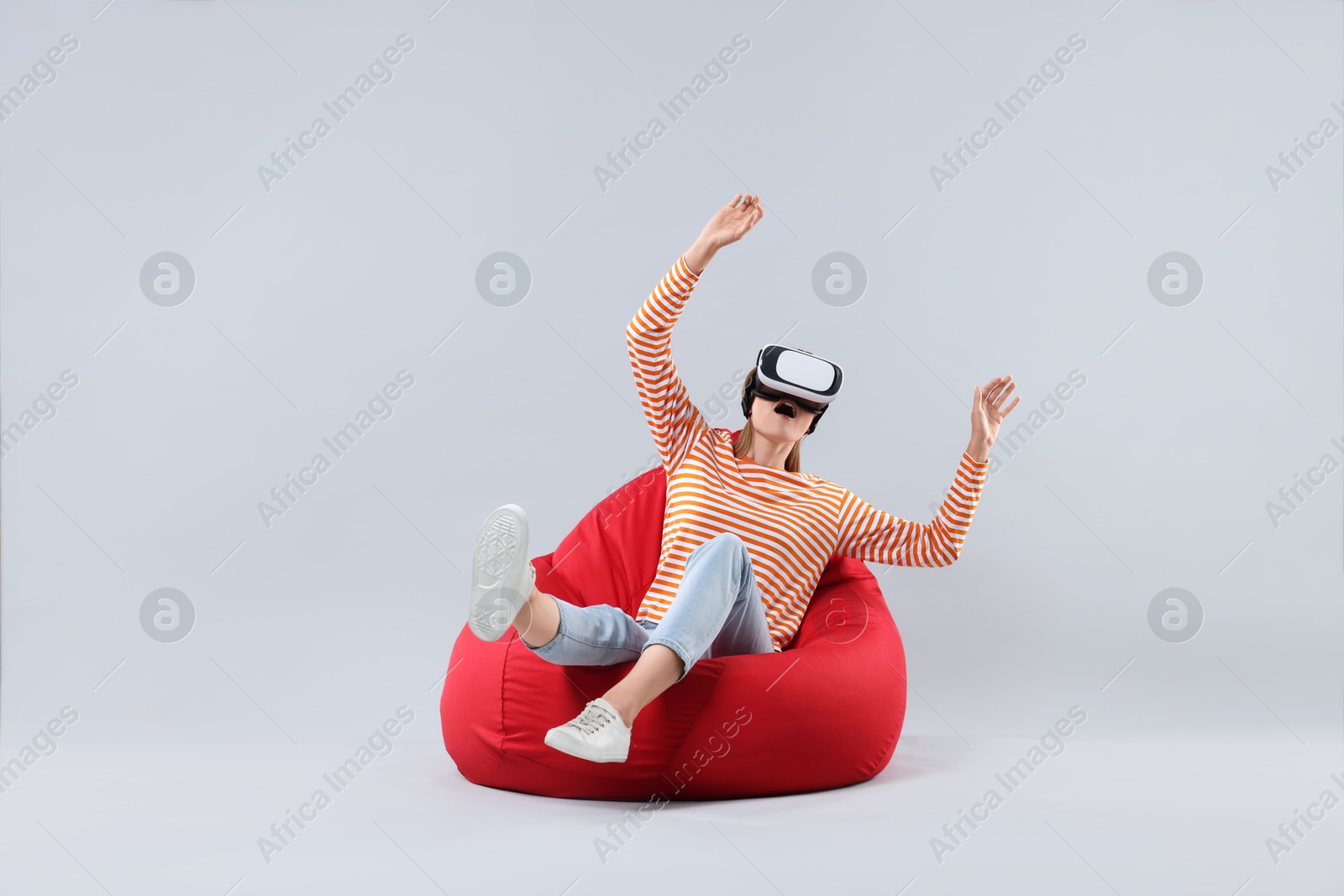 Photo of Emotional woman with virtual reality headset sitting on bean bag chair against gray background