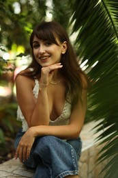 Smiling woman sitting near palm plants outdoors