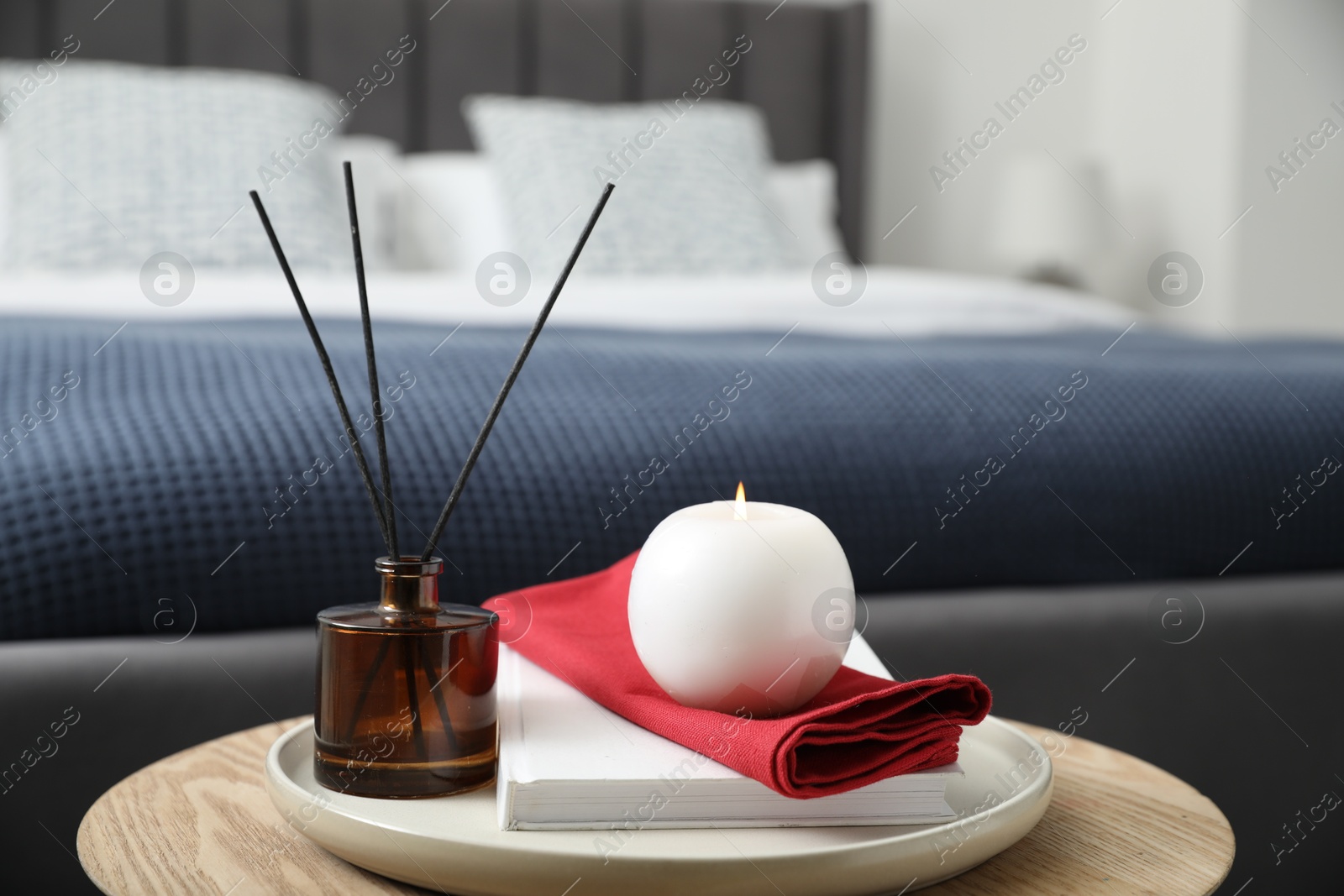 Photo of Burning candle, napkin, book and reed diffuser on wooden table indoors