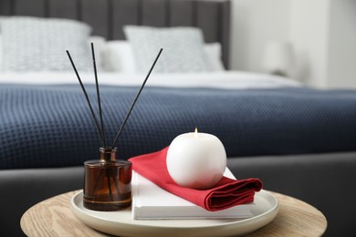 Photo of Burning candle, napkin, book and reed diffuser on wooden table indoors