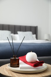 Burning candle, napkin, book and reed diffuser on wooden table indoors