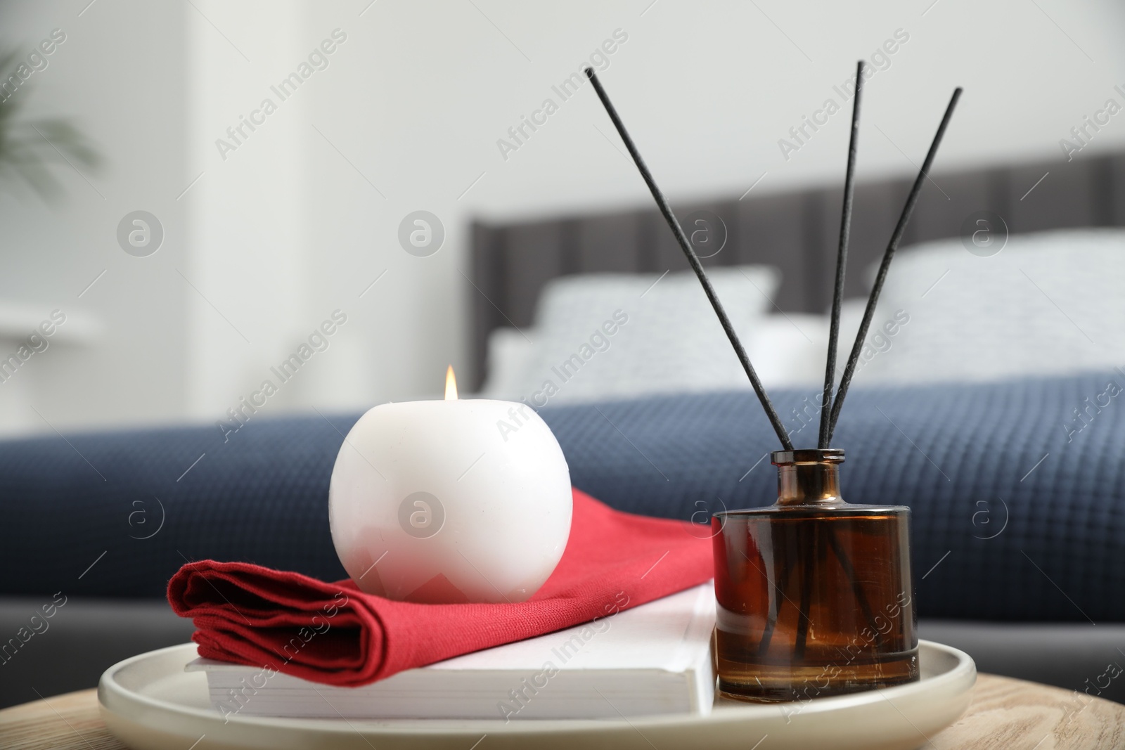 Photo of Burning candle, napkin, book and reed diffuser on wooden table indoors