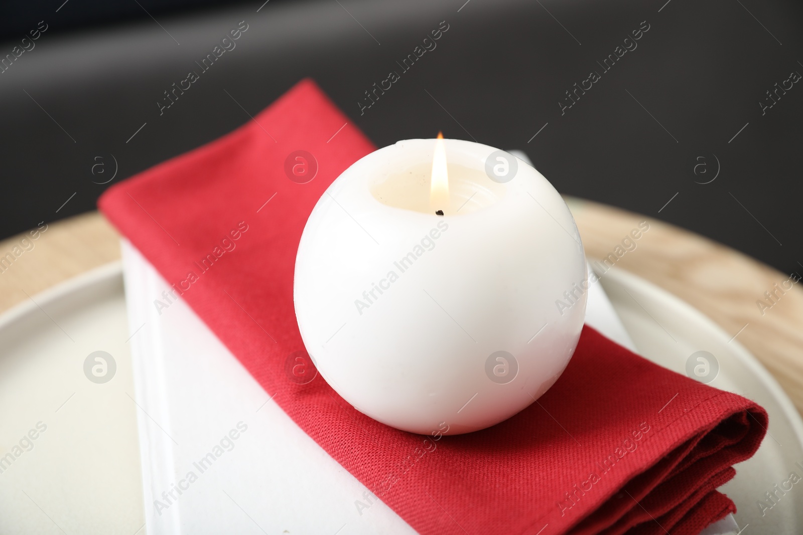 Photo of Burning candle and red napkin on table indoors, closeup