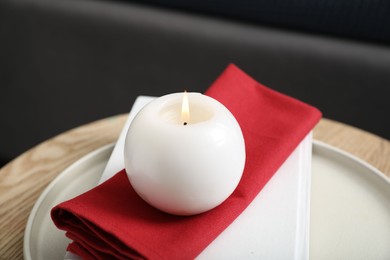 Burning candle and red napkin on wooden table indoors, closeup