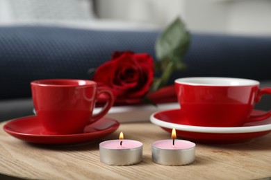 Burning candles, cups of drink and red rose on wooden table indoors