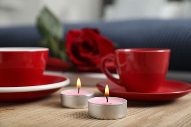 Burning candles, cups of drink and red rose on wooden table indoors