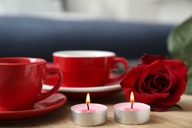 Photo of Burning candles, cups of drink and red rose on wooden table indoors, closeup