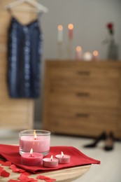 Photo of Burning candles, napkin and red paper hearts on wooden table indoors