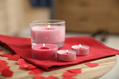 Burning candles, napkin and red paper hearts on wooden table indoors, closeup