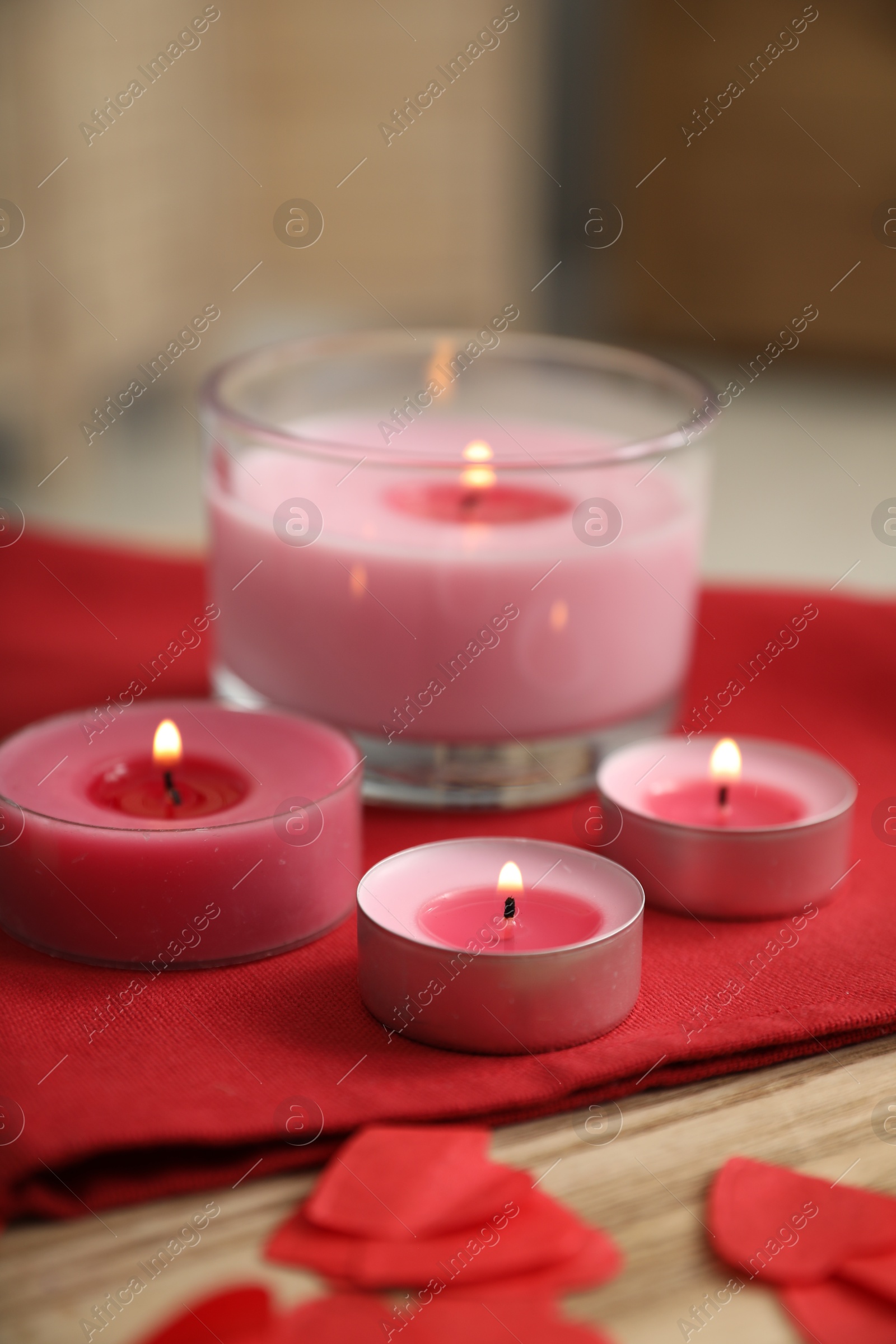 Photo of Burning candles, napkin and red paper hearts on wooden table indoors, closeup