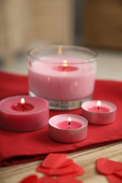 Burning candles, napkin and red paper hearts on wooden table indoors, closeup