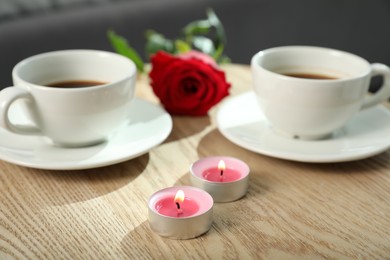 Photo of Burning candles, rose and cups of drink on wooden table indoors, closeup