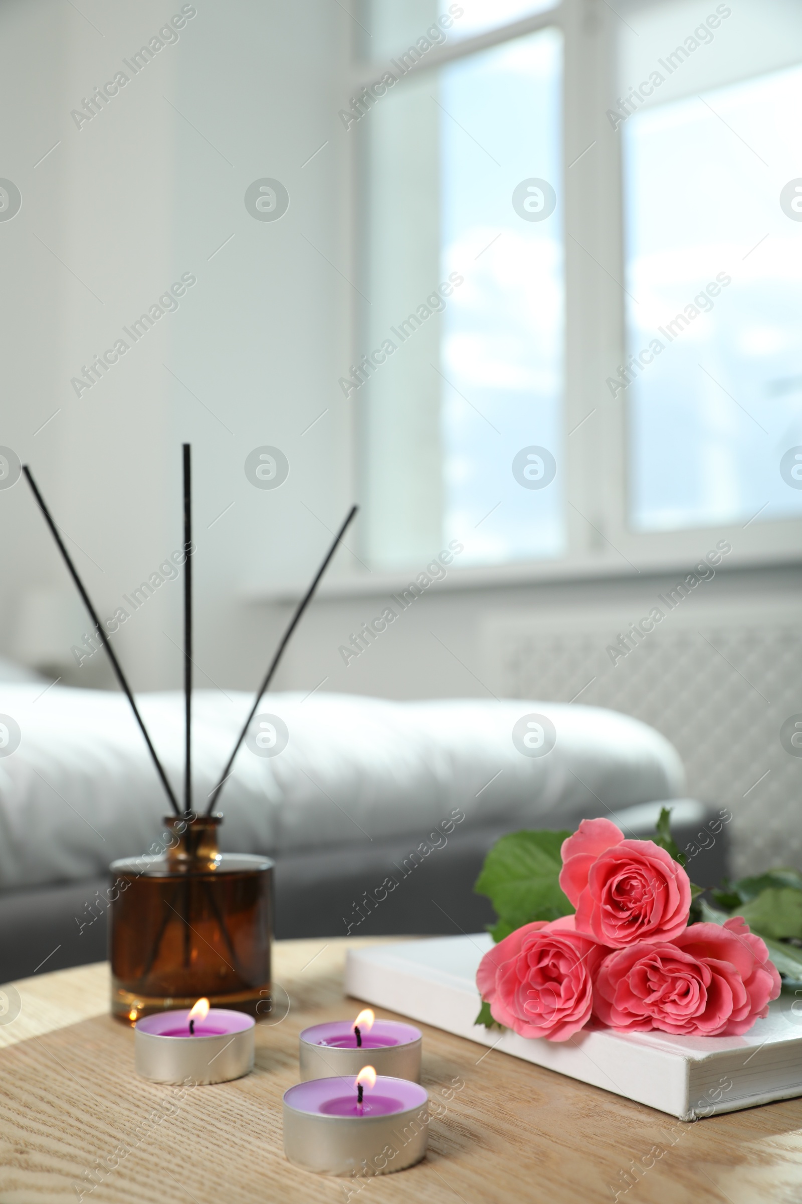 Photo of Burning candles, rose flowers, book and reed diffuser on wooden table indoors