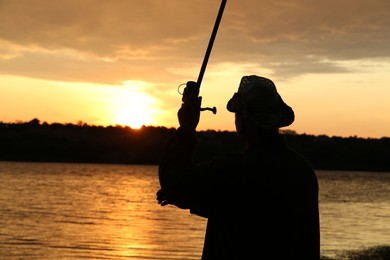 Fisherman with rod fishing near lake at sunset, back view