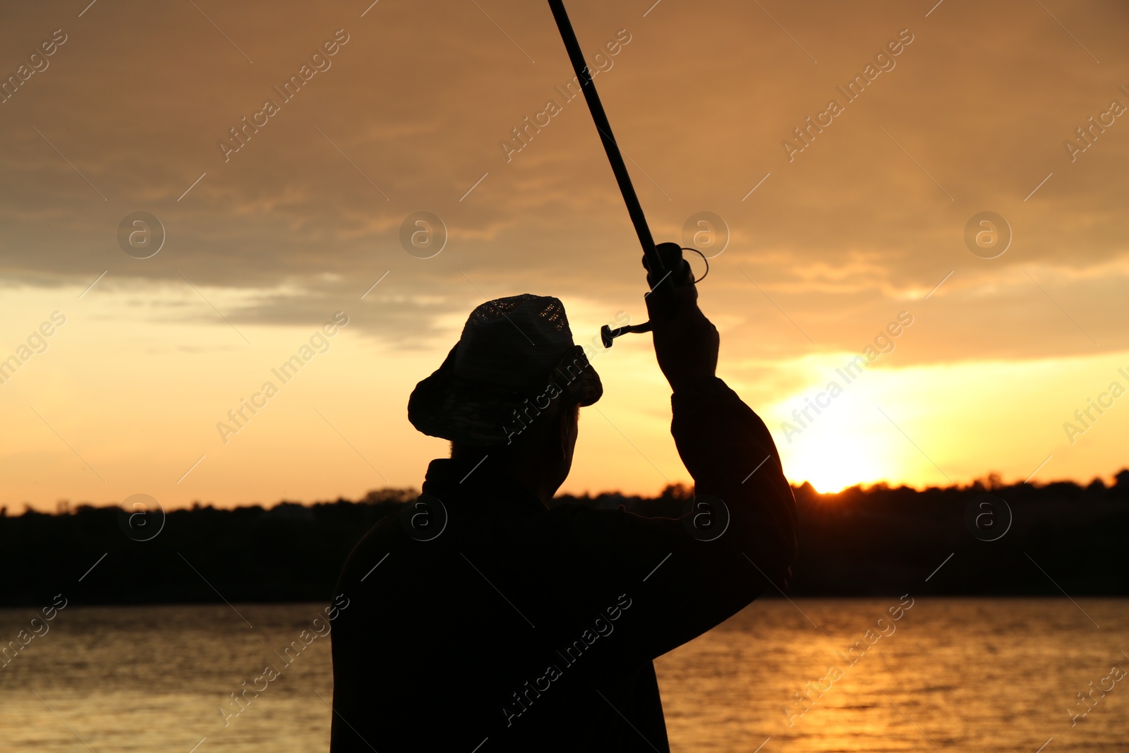 Photo of Fisherman with rod fishing near lake at sunset, back view