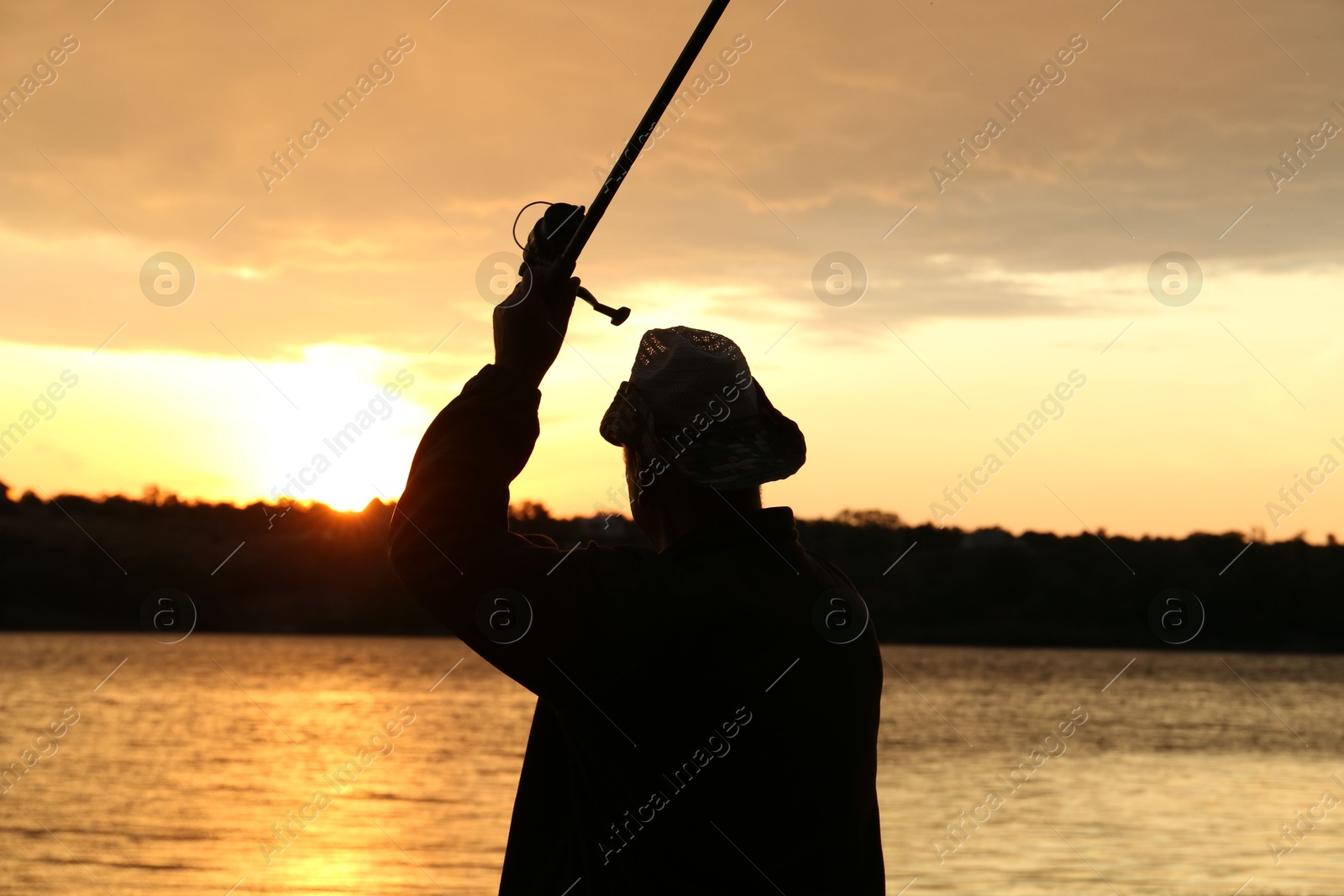 Photo of Fisherman with rod fishing near lake at sunset, back view