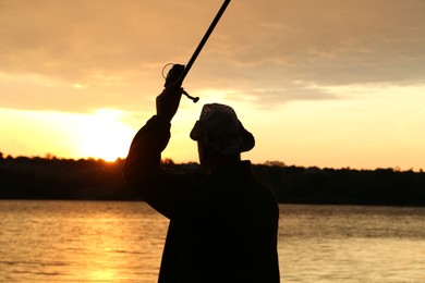 Fisherman with rod fishing near lake at sunset, back view