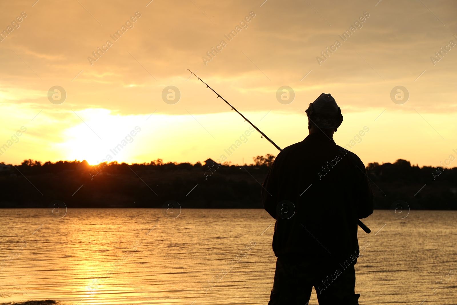 Photo of Fisherman with rod fishing near lake at sunset. Space for text