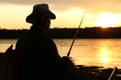 Fisherman with rod fishing near lake at sunset, back view