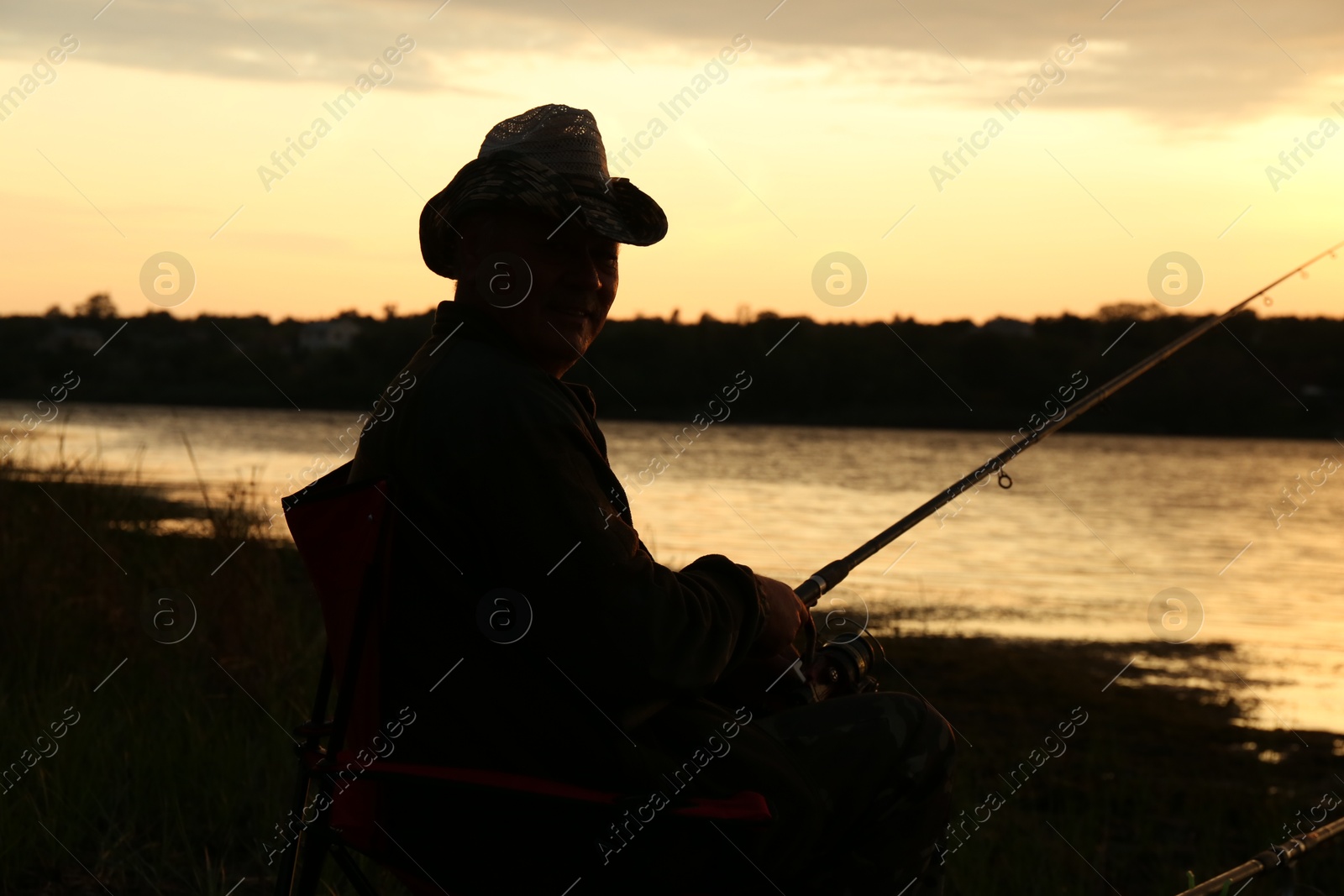 Photo of Fisherman with rod fishing near lake at sunset