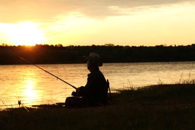 Fisherman with rod fishing near lake at sunset