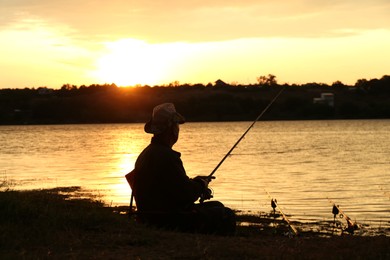 Fisherman with rod fishing near lake at sunset