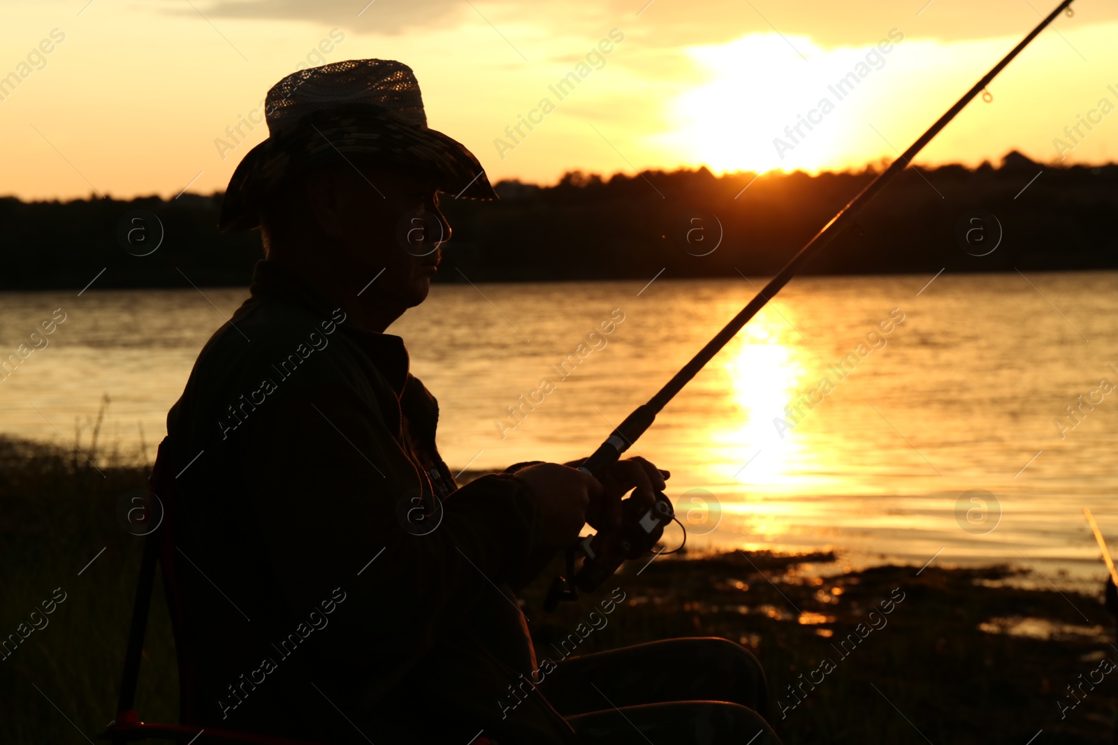 Photo of Fisherman with rod fishing near lake at sunset