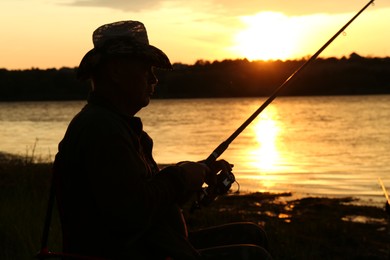 Fisherman with rod fishing near lake at sunset