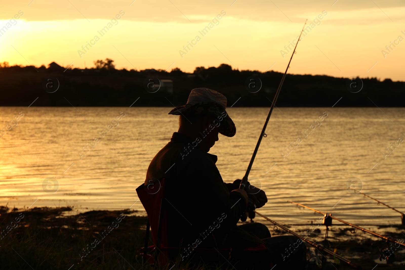 Photo of Fisherman with rod fishing near lake at sunset