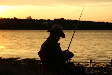 Photo of Fisherman with rod fishing near lake at sunset