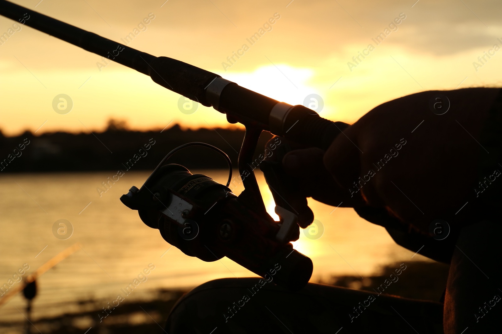 Photo of Fisherman with rod fishing near lake at sunset, closeup