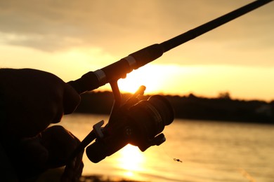 Fisherman with rod fishing near lake at sunset, closeup